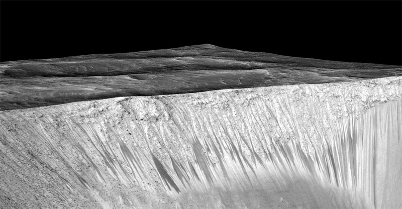 Dark narrow streaks called recurring slope lineae emanate out of the walls of Garni crater on Mars. The dark streaks here are up to few hundred meters in length. They are hypothesised to be formed by flow of briny liquid water on Mars.